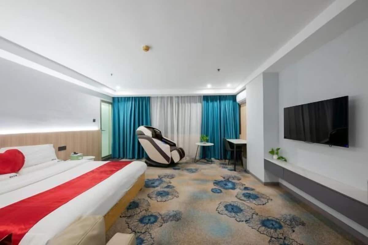 A hotel room with a bed, a massage chair, a small table, and a TV on the wall.