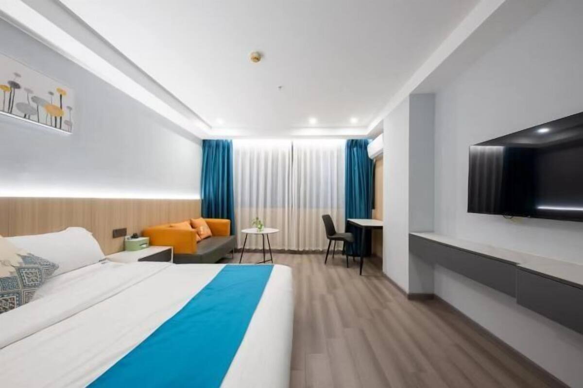 A modern hotel room with a bed, a desk, a chair, a TV, and a window with curtains.