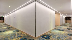 A hotel corridor with a central partition, recessed lighting, and a floral carpet.