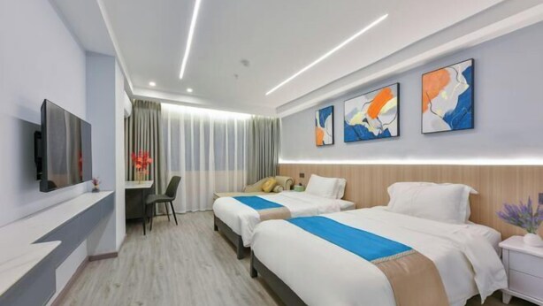 A hotel room with two beds, a desk, a chair, a TV, and abstract artwork on the wall.