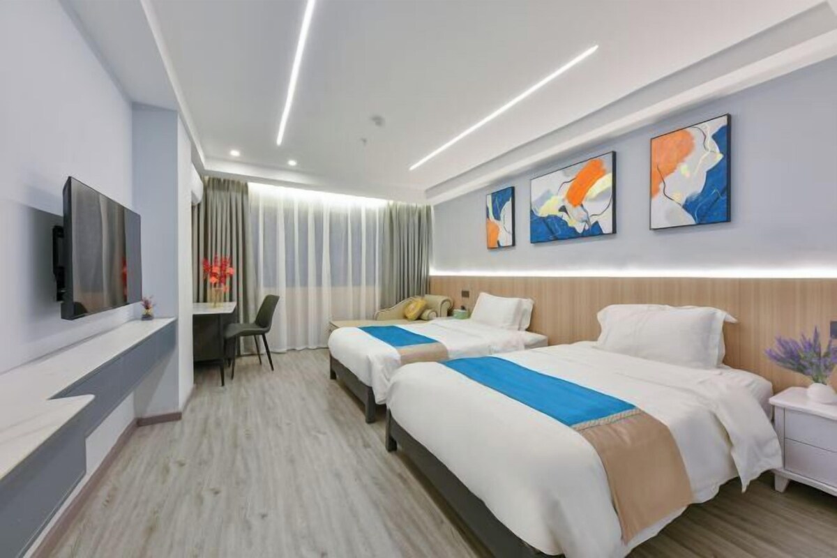 A hotel room with two beds, a desk, a chair, a TV, and abstract artwork on the wall.