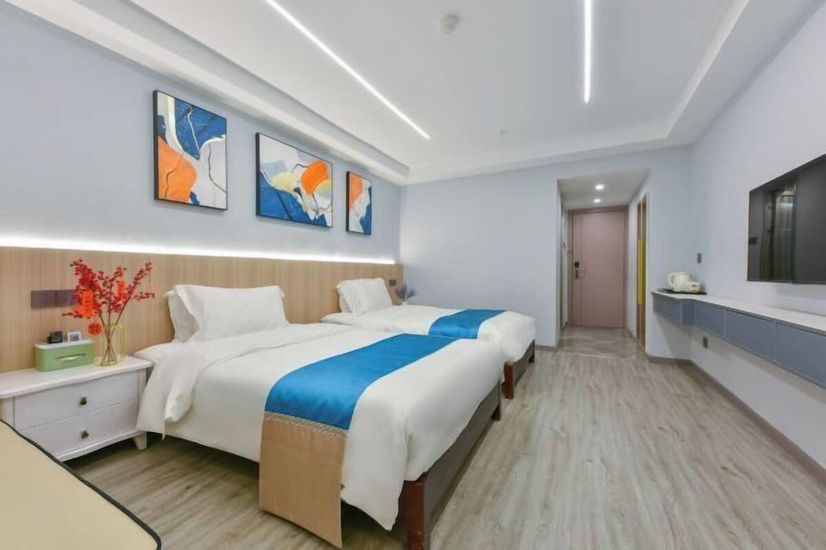 A hotel room with two beds, a bedside table, a TV, and abstract wall art.