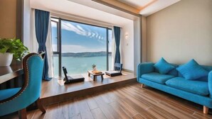A room with a large window, a blue sofa, a wooden floor, and a small table with a plant. - Piaoyang Guohai Guesthouse (Zhoushan)