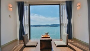 A room with a large window, two chairs, a small table, and a view of the sea. - Piaoyang Guohai Guesthouse (Zhoushan)