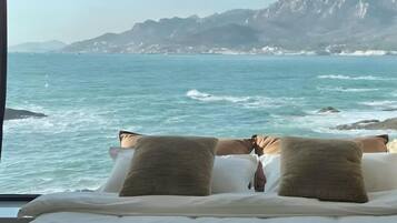A bed with pillows facing a coastal view.