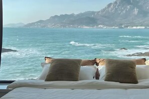 A bed with pillows facing a coastal view.