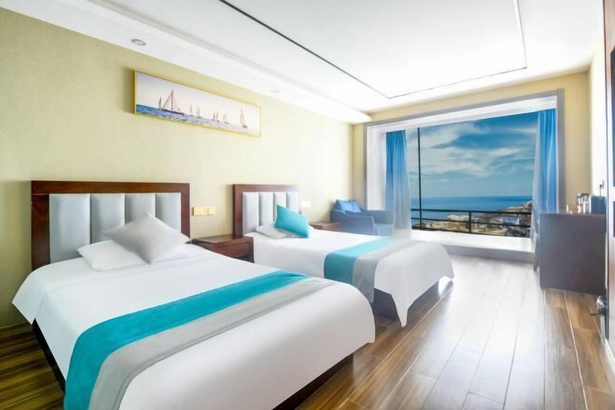 A hotel room with two beds, a large window with a view, and a painting on the wall.