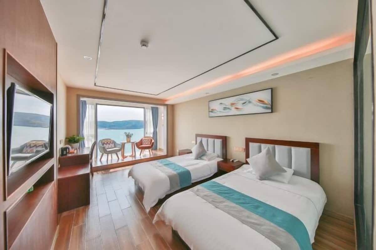 A hotel room with two beds, a large window with a view, a small table, and a chair.