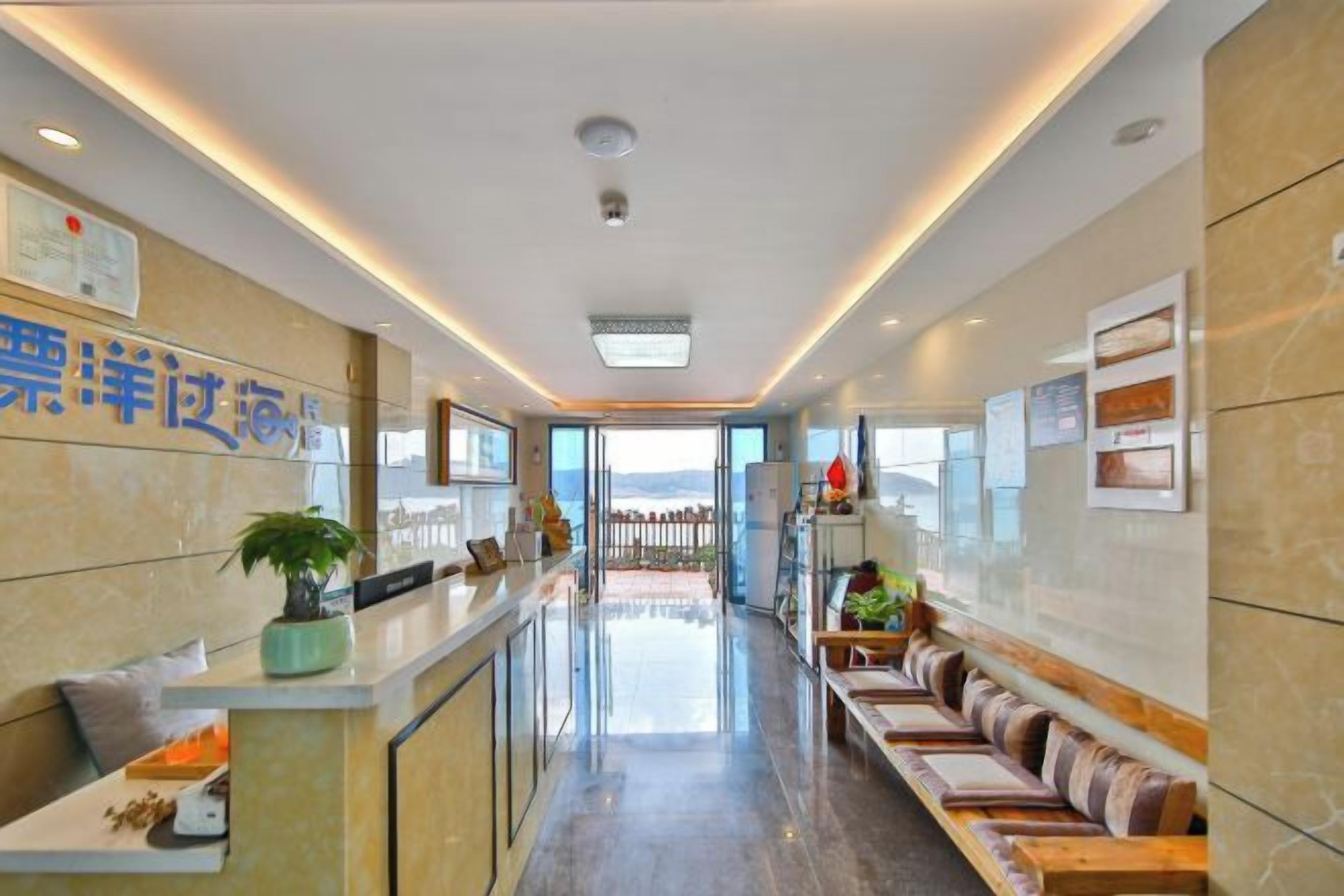 A hotel reception area with a long counter, seating, and a view through the glass doors.