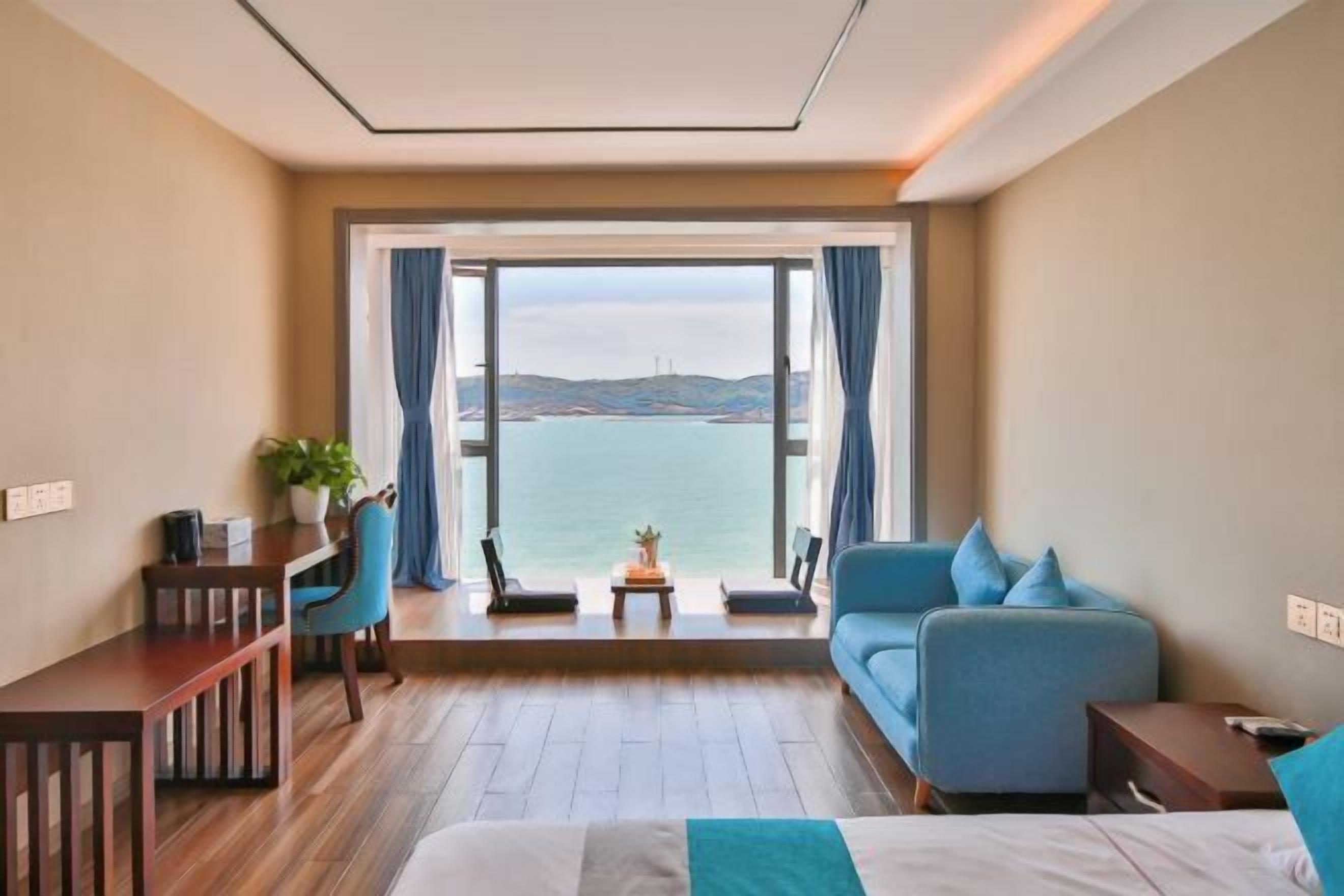 A hotel room with a bed, a desk, a chair, a sofa, and a view of the sea.