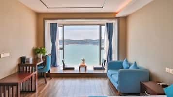 A hotel room with a bed, a desk, a chair, a sofa, and a view of the sea.