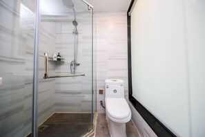 A modern bathroom with a glass-enclosed shower, a white toilet, and a small shelf with toiletries. - Piaoyang Guohai Guesthouse (Zhoushan)