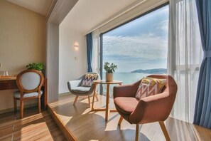 A room with a large window, two chairs, a small table, and a desk with a plant. - Piaoyang Guohai Guesthouse (Zhoushan)