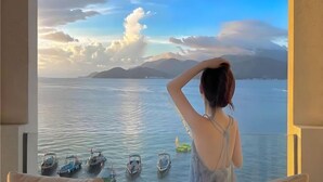 A room with a view of boats on the water, a balcony, and a person standing by the window. - Piaoyang Guohai Guesthouse (Zhoushan)