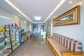 A hotel lobby with a reception desk, a long bench, and a staircase leading to the upper floors. - Piaoyang Guohai Guesthouse (Zhoushan)