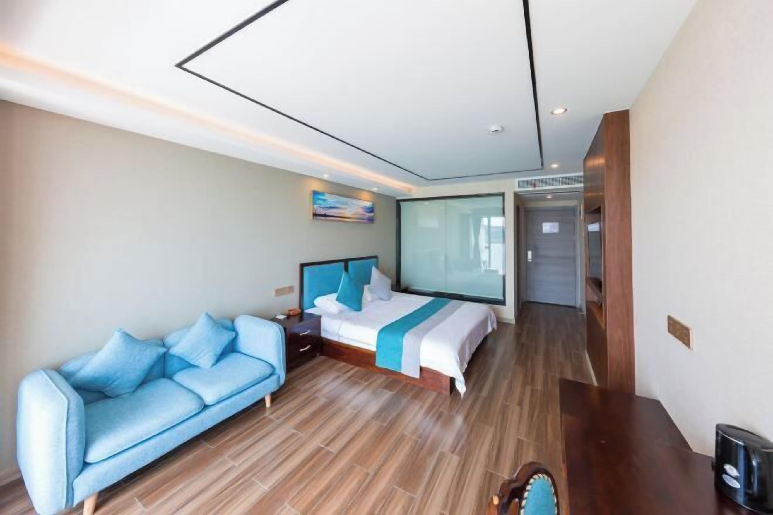 A modern hotel room with a bed, a sofa, a nightstand, and a large window.