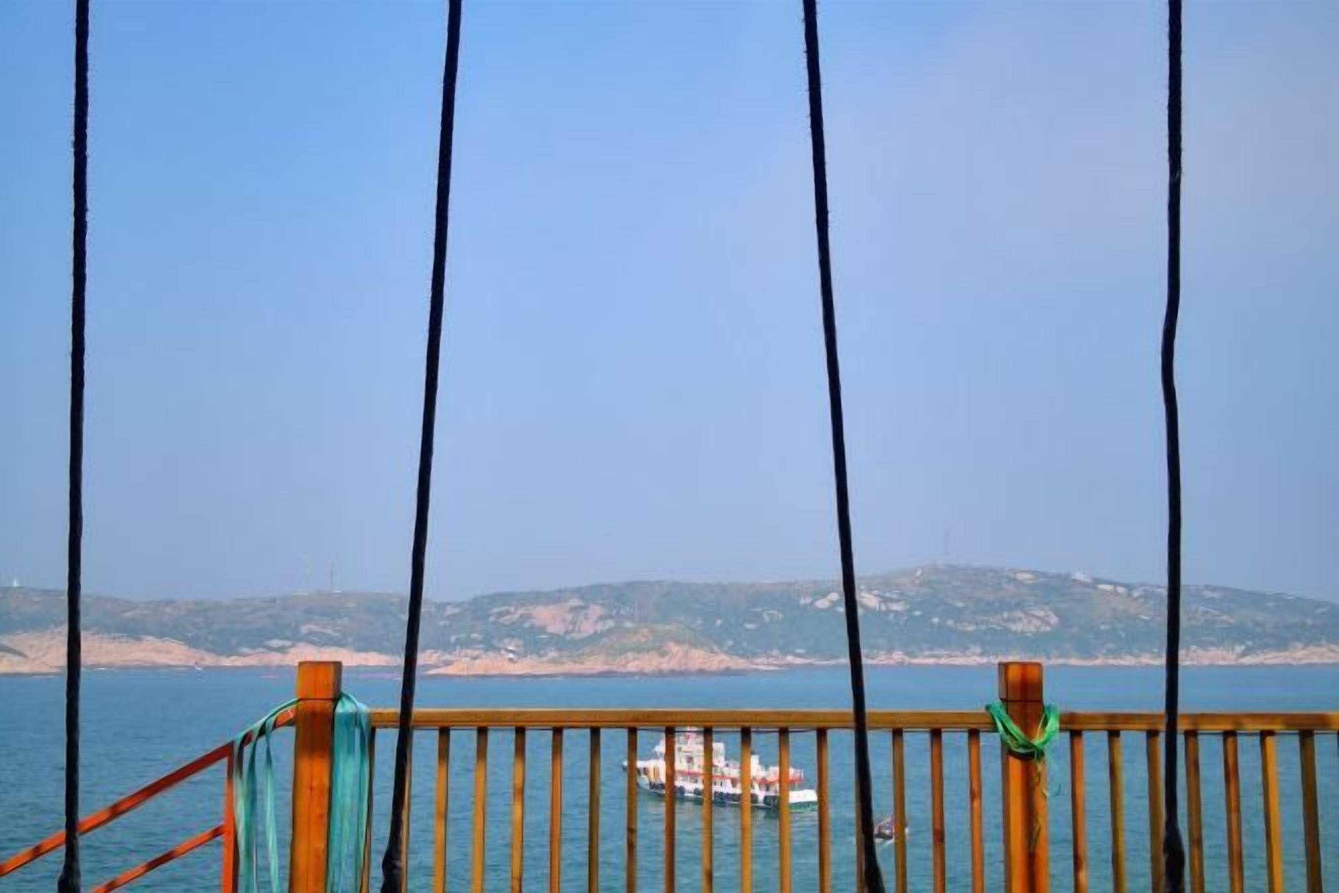 Ringhiera in legno con vista su una barca sull'acqua e una costa in lontananza.