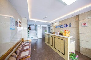 A hotel reception area with a reception desk, seating area, and a staircase leading to another floor. - Piaoyang Guohai Guesthouse (Zhoushan)