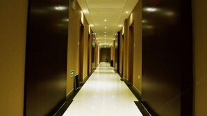 Een lange, smalle hotelgang met een glanzende vloer en donkere muren.