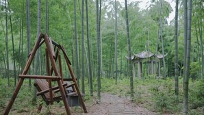 Een houten schommel in een bamboebos, met een pad dat naar een traditionele constructie leidt.
