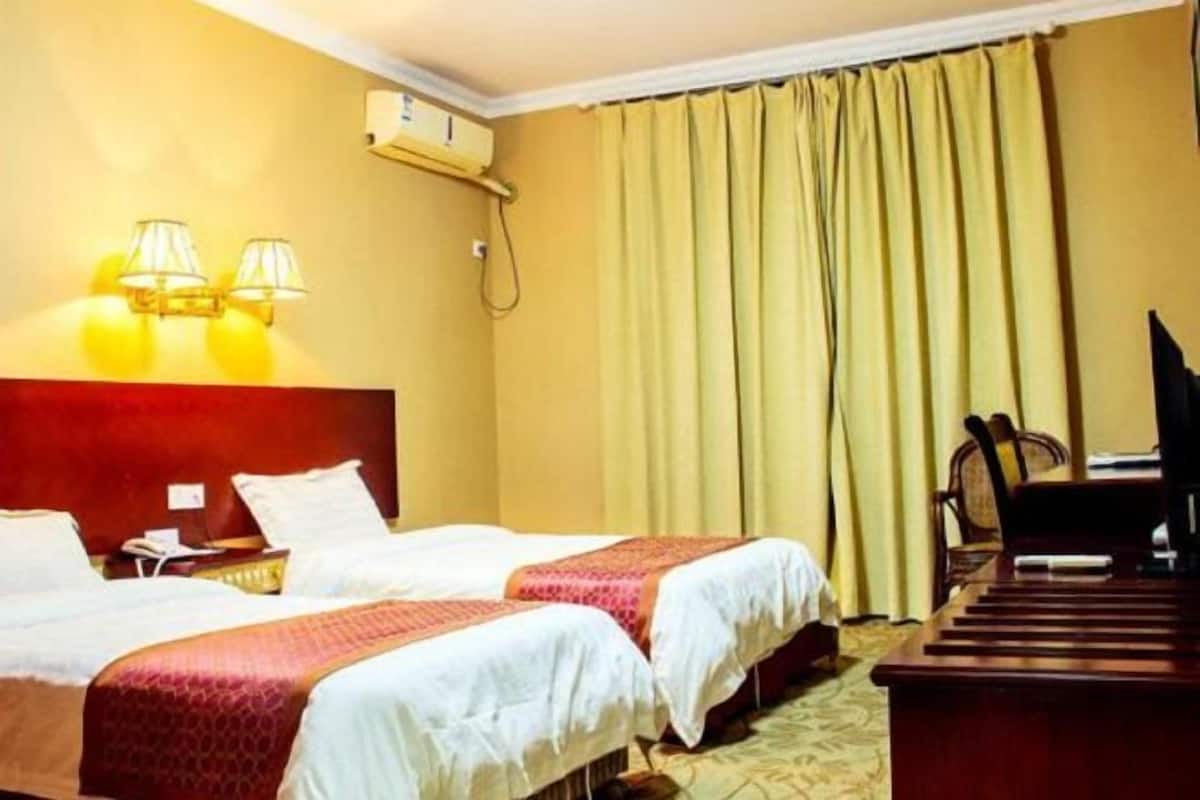 Une chambre d’hôtel avec deux lits, un bureau en bois, une télévision et une fenêtre avec des rideaux.