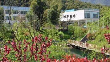 A modern building with a sign, surrounded by lush greenery and a small bridge over a body of water.