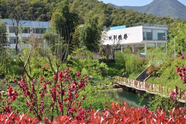 A modern building with a sign, surrounded by lush greenery and a small bridge over a body of water. - Jingya Bieyuan Hotel (Liyang)