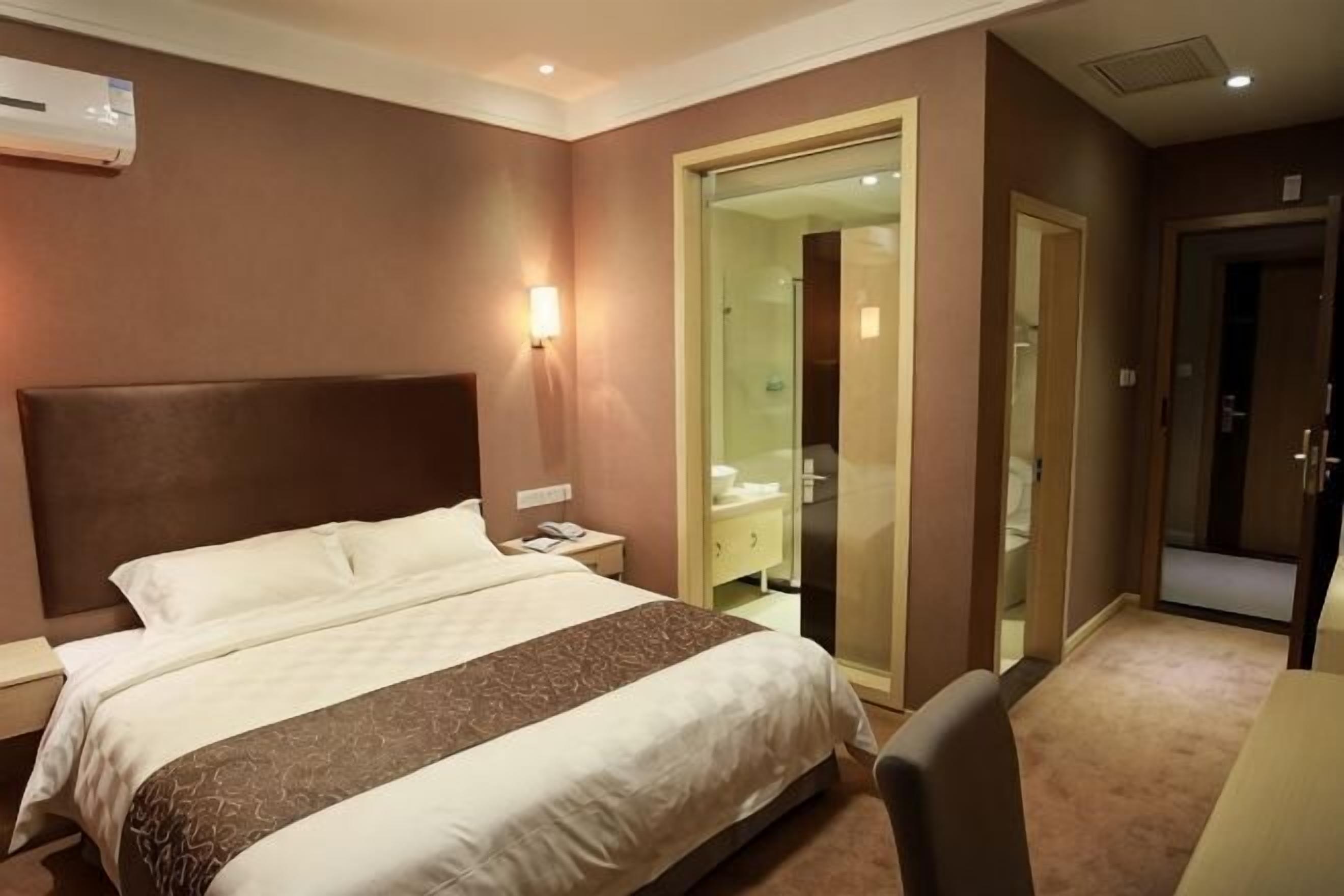 Ein Hotelzimmer mit einem großen Bett, einem Nachttisch und einer Glastür zum Badezimmer.