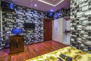 A room with a checkered wall pattern, a wooden floor, a television, a door, and a table with microphones. - Jingya Bieyuan Hotel (Liyang)