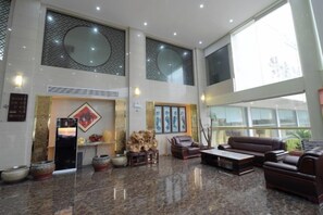 A spacious lobby with a high ceiling, large windows, and a mix of seating areas including sofas and chairs. - Jingya Bieyuan Hotel (Liyang)