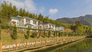 Una hilera de casas junto a un lago tranquilo, con un puente de madera, rodeado de árboles y colinas.