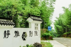 Um portão chinês tradicional com caracteres, uma estrada e vegetação exuberante.
