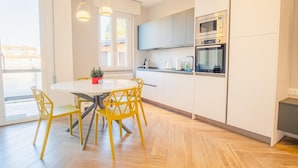 A modern kitchen with white cabinets, a microwave, and an oven. There is a dining table with yellow chairs and a potted plant on it. - The Roman Villa View - Italian Homing (Desenzano del Garda)