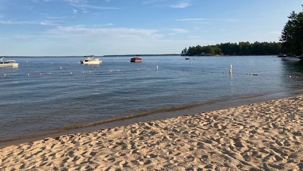 A beach with calm waters, boats, and a forested area in the background.