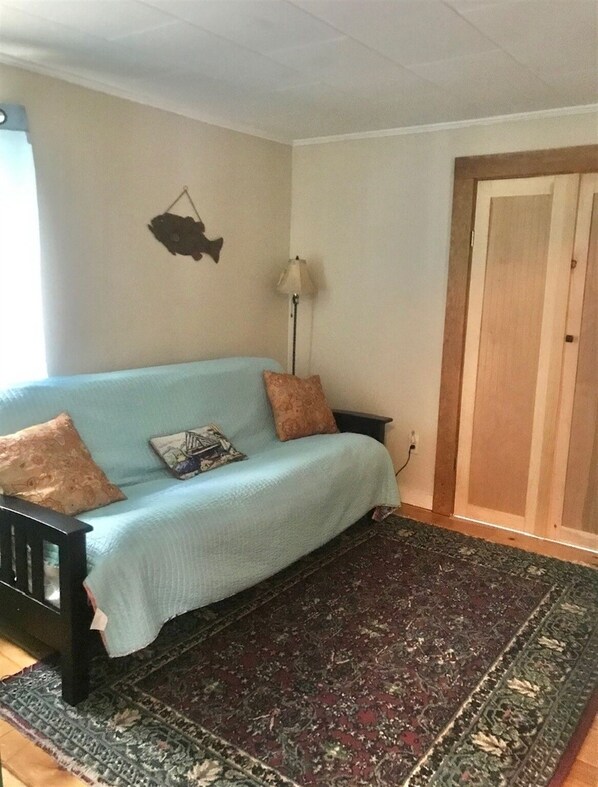 Ein Zimmer mit einem hellblauen Sofa, zwei gemusterten Kissen, einem dunklen Teppich mit Muster, einer Wanddekoration im Fischdesign, einer Stehlampe und einer Holztür.