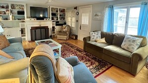 A spacious living room with a grey sofa, a blue sofa, and a small table. There is a television on a stand and a fireplace.