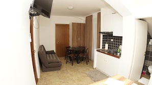 Una cocina compacta con comedor, un sofá y un televisor montado en la pared.
