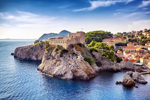 A coastal town with a historic stone fortress on a rocky outcrop, surrounded by lush greenery and traditional buildings with red-tiled roofs. - Inviting Apartment 14 Sleeps 3 Guests (Split)