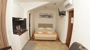 Una habitación pequeña y estrecha con una cama, una kitchenette y un cuadro en la pared.