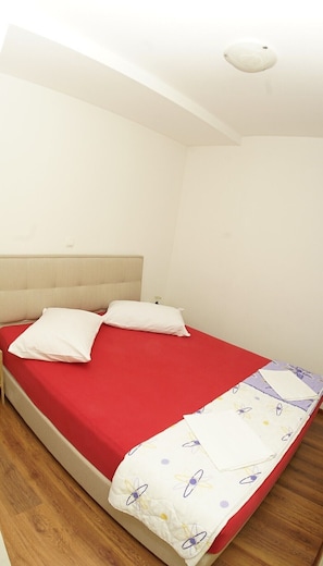 A single bed with a red mattress and white pillows in a room with white walls and a wooden floor.