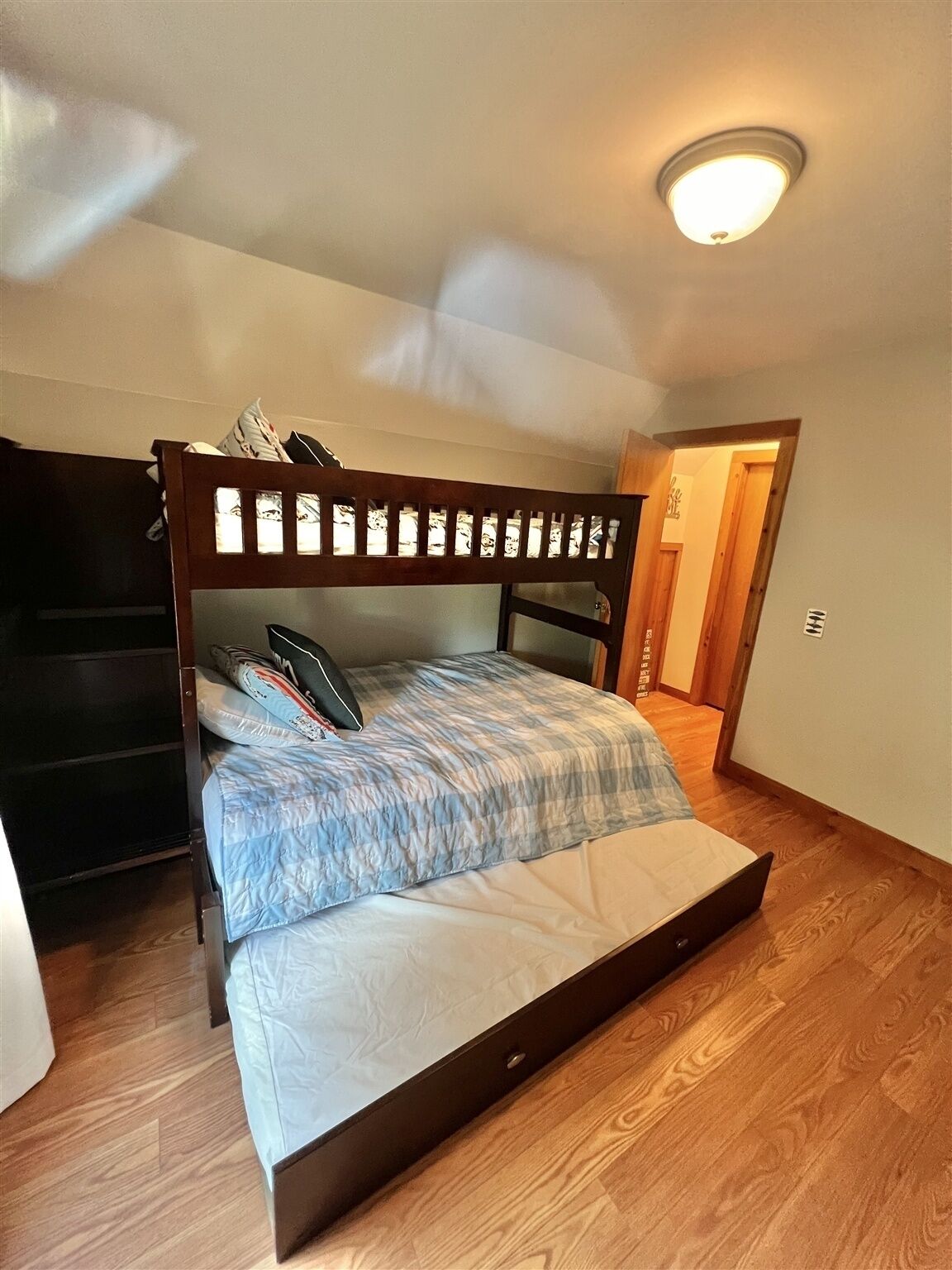 Ein Einzelbett mit Holz-Kopfschild in einem Zimmer mit Holzboden und einer Deckenleuchte.