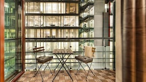 Un espacio interior moderno con piso de diseño encalado, una mesa de madera con dos sillas y grandes ventanales que ofrecen vistas a una zona industrial.