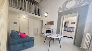 A modern living room with a blue sofa, a dining table with a patterned tablecloth, and a kitchen visible through an open doorway. - Elegant apartment with Parking, A/C, Wi-Fi, in the old town (Pistoia)