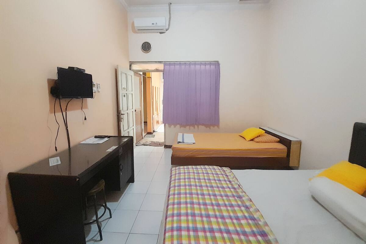 A hotel room with a bed, a desk, a television, and an air conditioning unit.