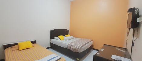 A small, compact room with two beds, one with a striped yellow and white bedspread and the other with a checkered bedspread. There is a desk with a chair and a telephone mounted on the wall.