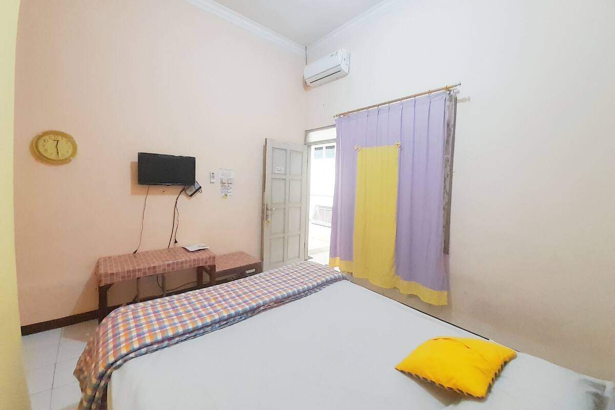 A bedroom with a bed, a small table, a television, and a window with curtains.
