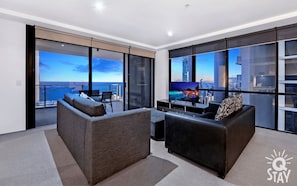 Relax in style with a panoramic city view from the comfort of this spacious living room, featuring a large sofa and flat-screen TV.