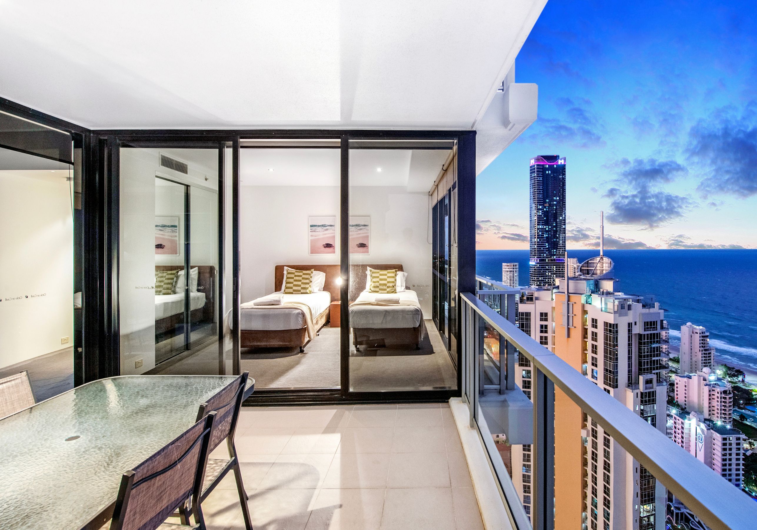 A balcony with a city view, two beds, a glass door, and a dining area.