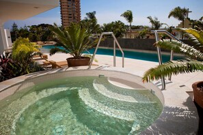 Relax by the serene pool surrounded by lush tropical plants and modern poolside seating.