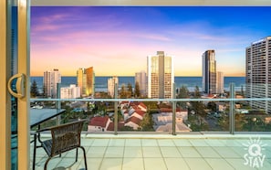 Enjoy breathtaking views of the city skyline from this balcony with a wicker chair and glass railing.